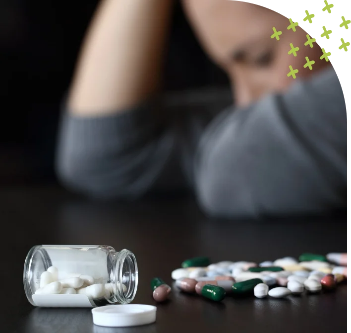 Pills scattered on table with sad person in background
